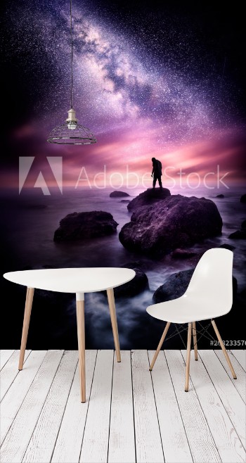 Picture of Night time Sea landscape with the Milky Way A man stands on a rocky shore line with the stars above him Photo composite